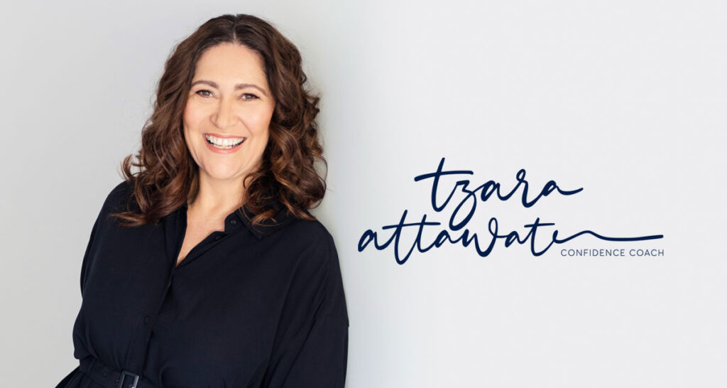 Tzara leaning against grey wall smiling with Tzara Attwater confidence coach written